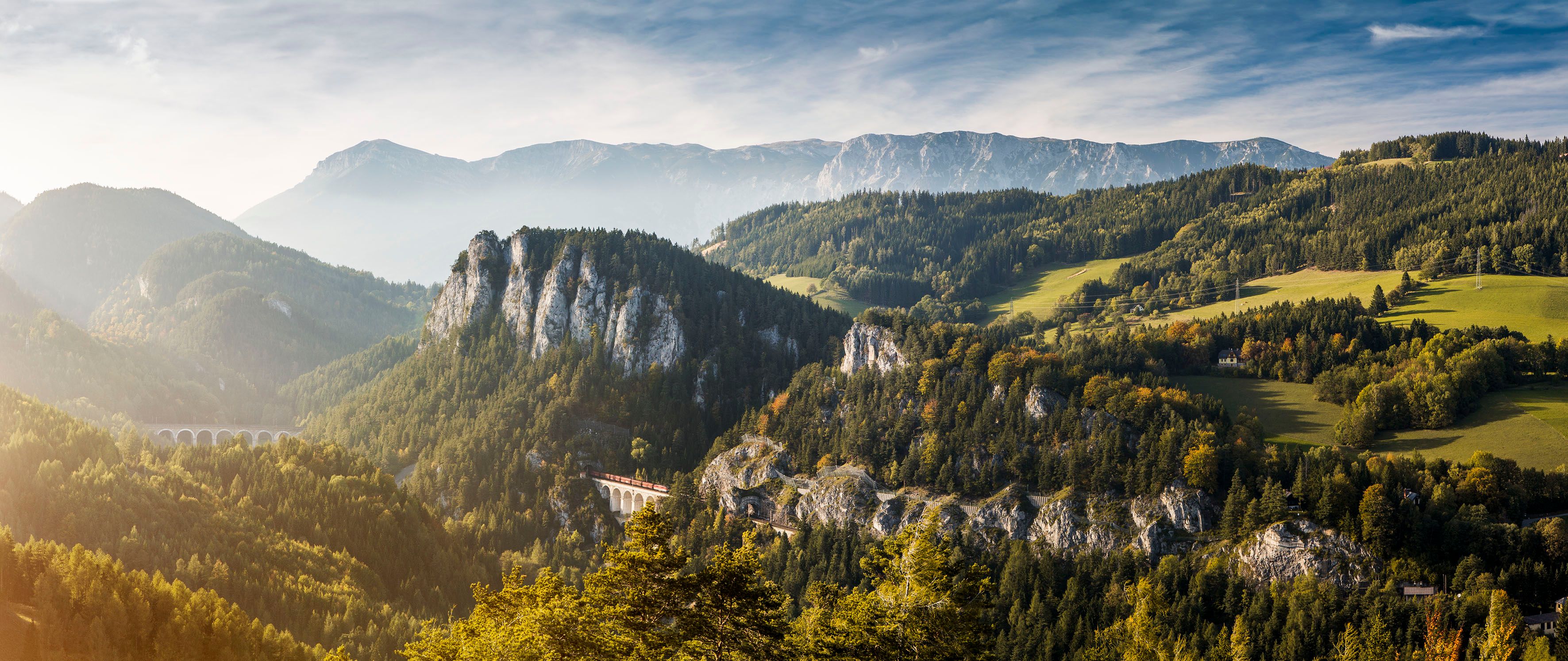 Panoramic view of the Semmering Railway in a mountainous landscape with forests and a viaduct.