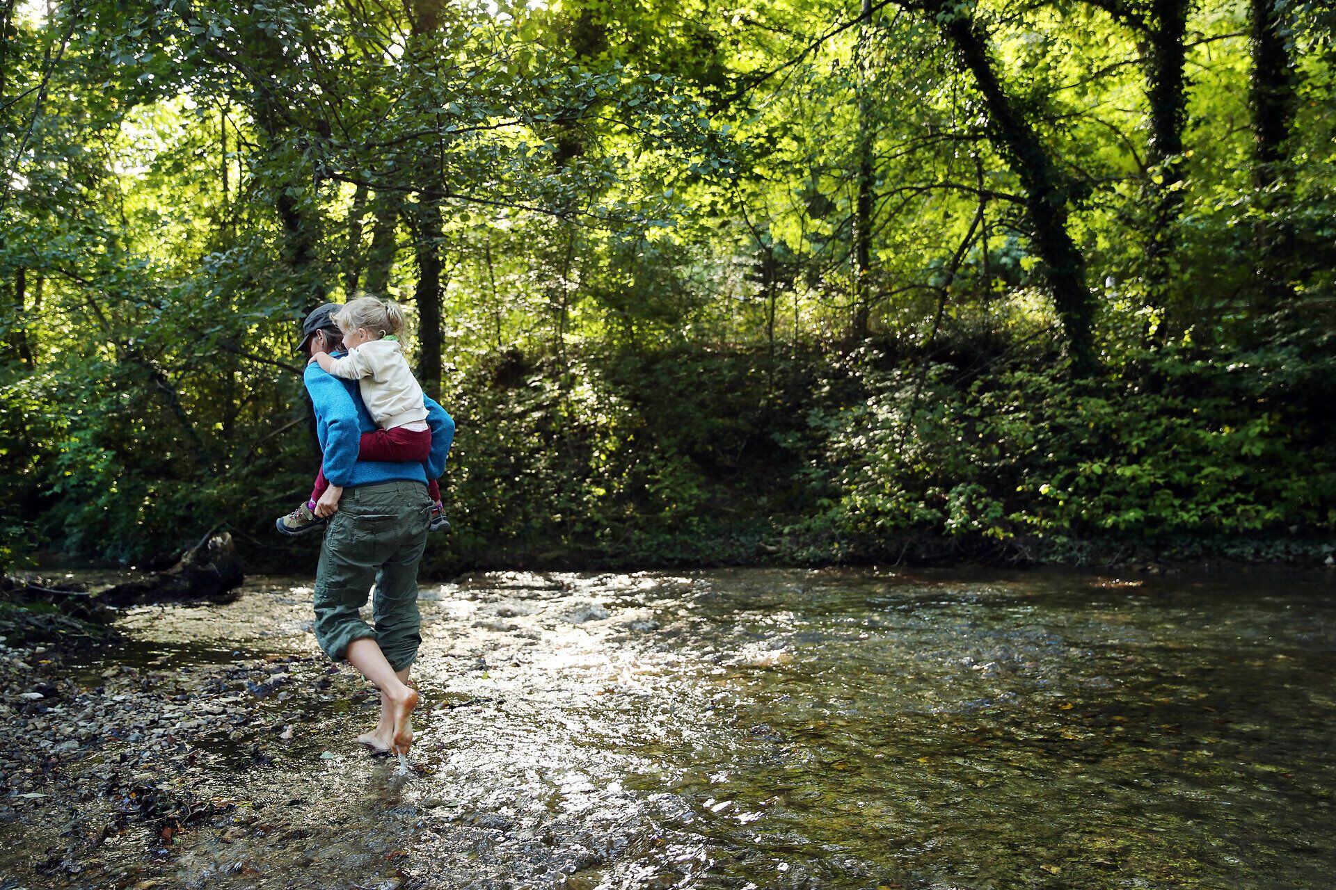 Eine Frau watet mit ihrem Kind am Rücken durch einen Bach im Naturpark Sierningtal.