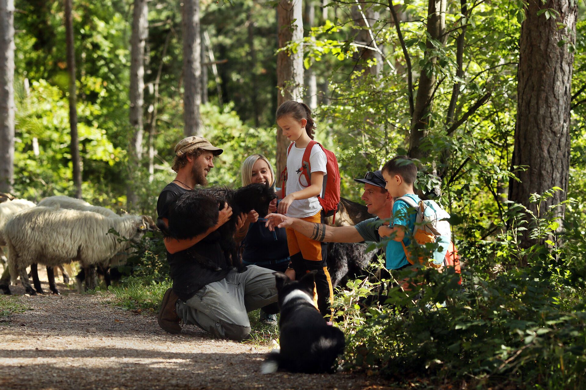 Ein Hirte hält eine Ziege fest während eine Familie rund um ihn sitzt und die Ziege streichelt. 