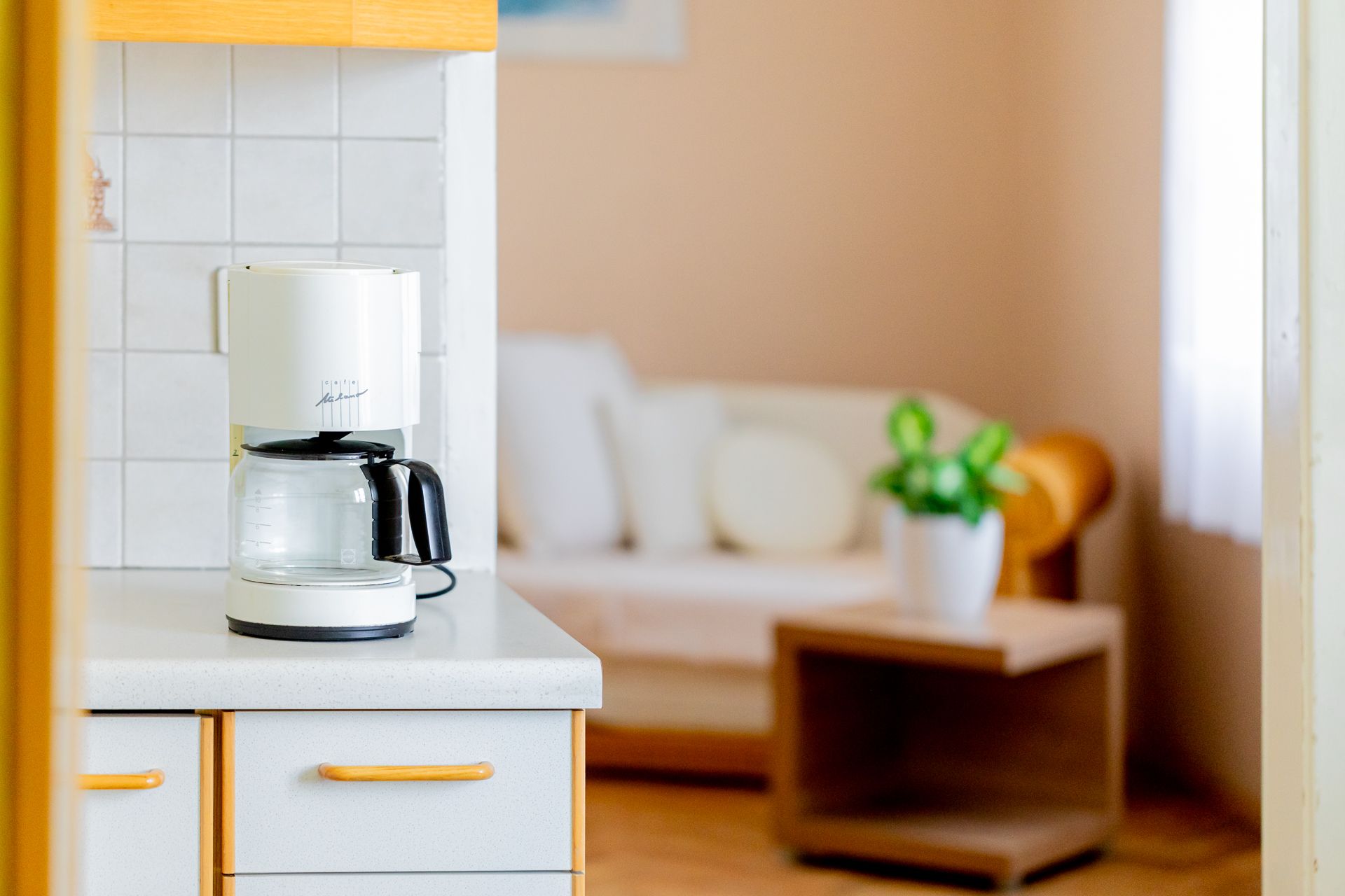 Kaffeemaschine auf Küchentheke mit Wohnzimmer im Hintergrund.