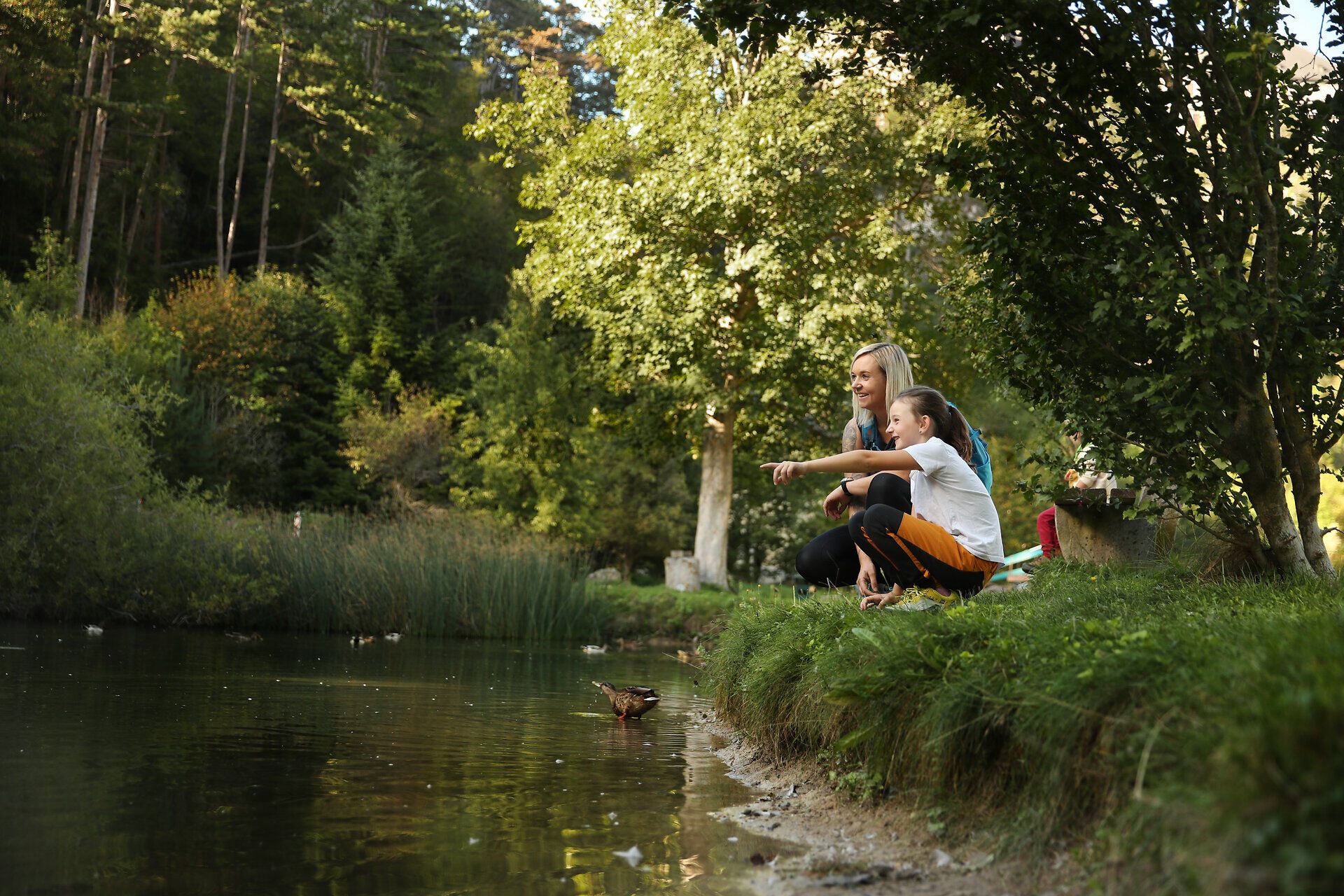 Eine Frau und ihr Kind hocken am Rande eines Teichs im Naturpark Sierningtal. 