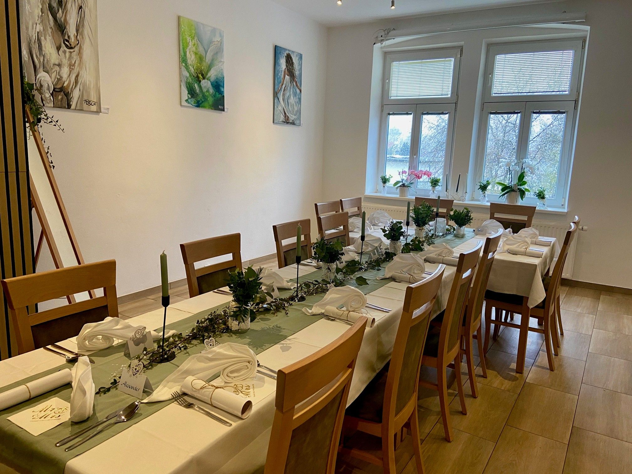 Ein festlich gedeckter Tisch in einem Raum mit Kunstwerken an der Wand und großen Fenstern.