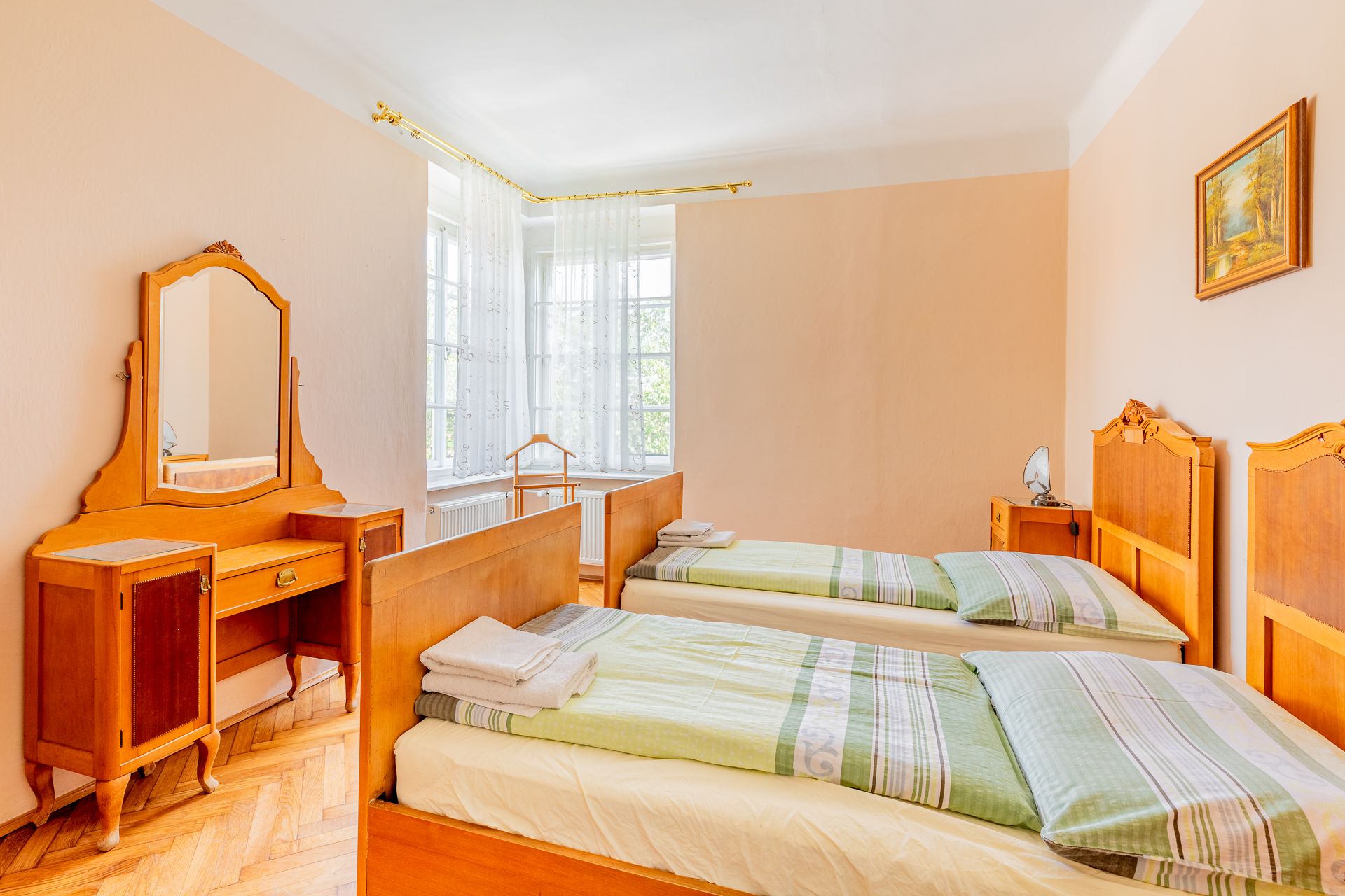 Ein traditionelles Schlafzimmer mit zwei Einzelbetten, einem Schminktisch mit Spiegel und einem Fenster mit weißen Vorhängen.