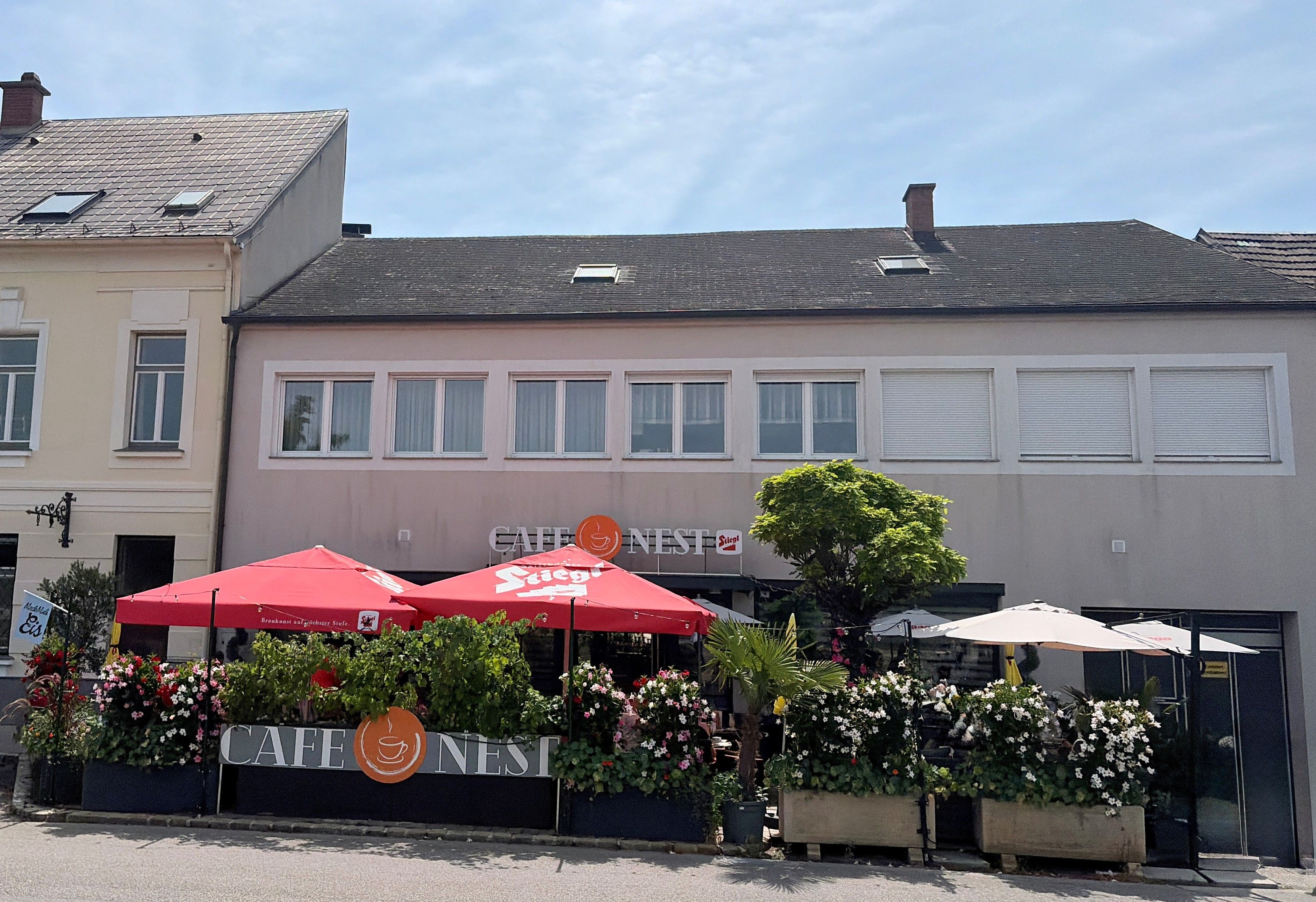 Exterior view of Cafe Nest in Ternitz, featuring red umbrellas and plants.