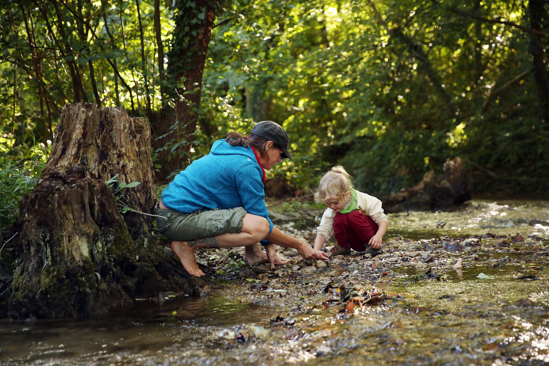 Eine Frau und ihr Kind spielen mit Steinen am Rand eines Baches im Naturpark Sierningtal. 
