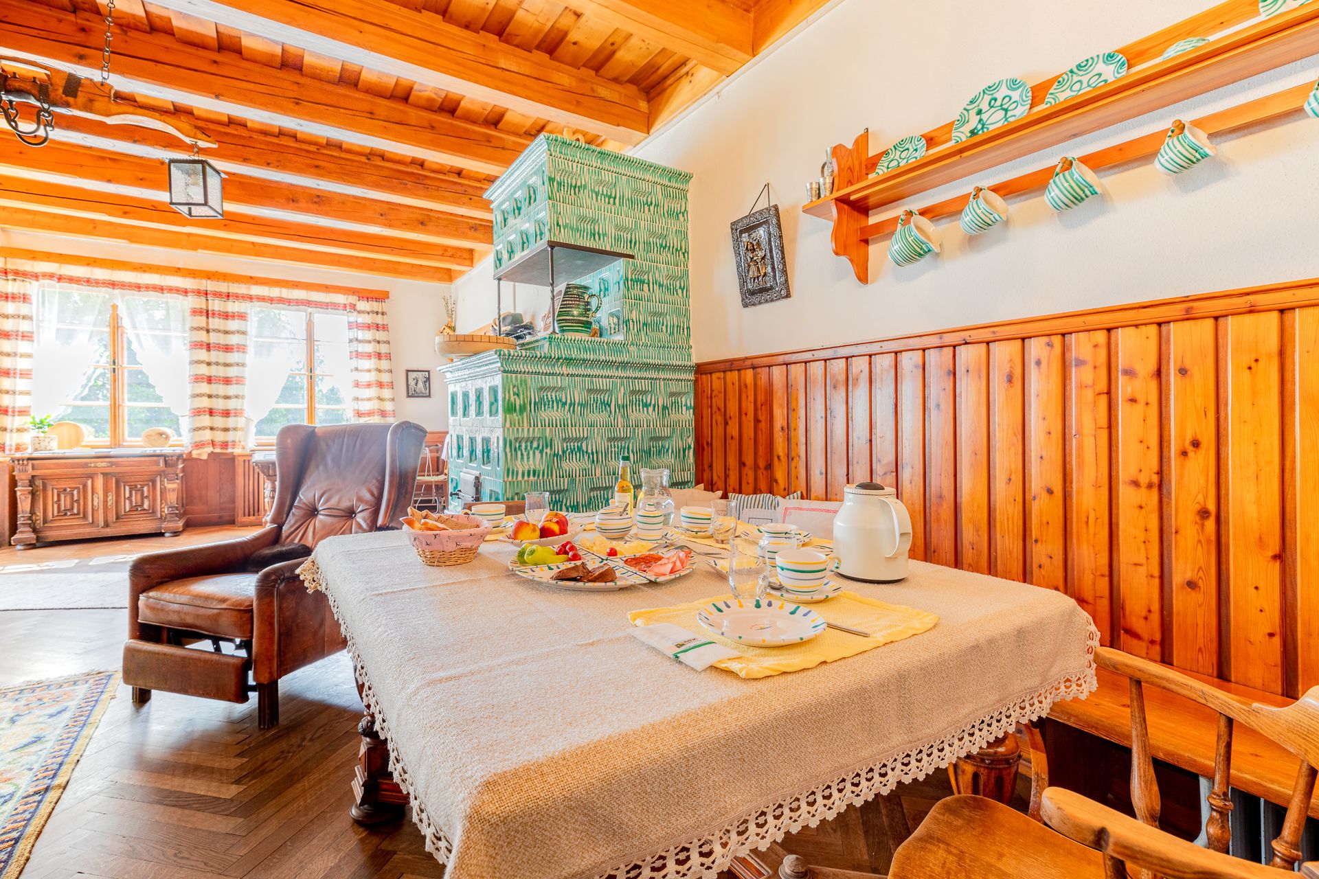 Gemütliches Esszimmer mit Holzmöbeln, gedecktem Tisch und grünem Kachelofen.