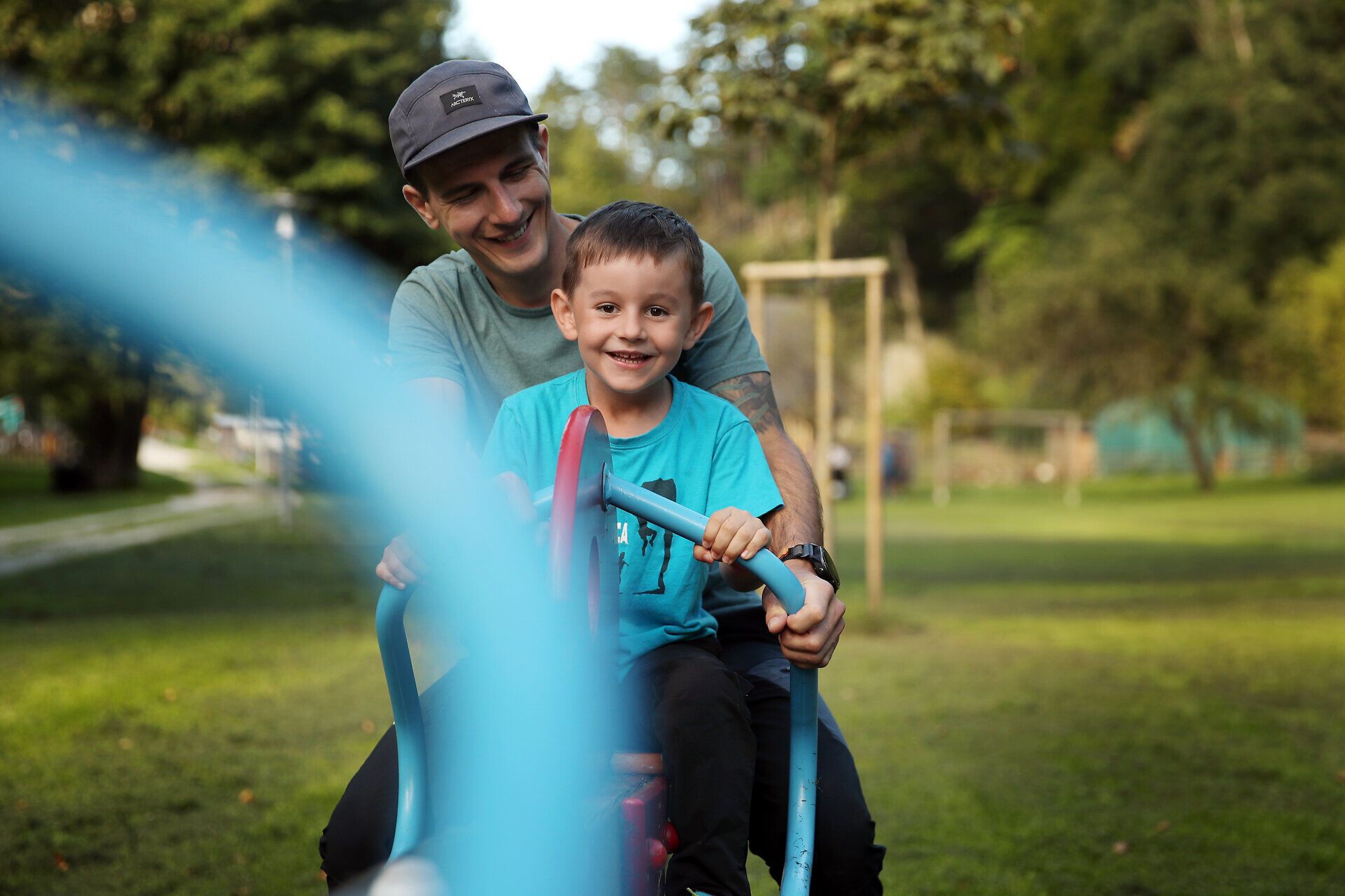 Ein Mann und sein Kind sitzen auf einem Spielgerät im Naturpark Sierningtal. 