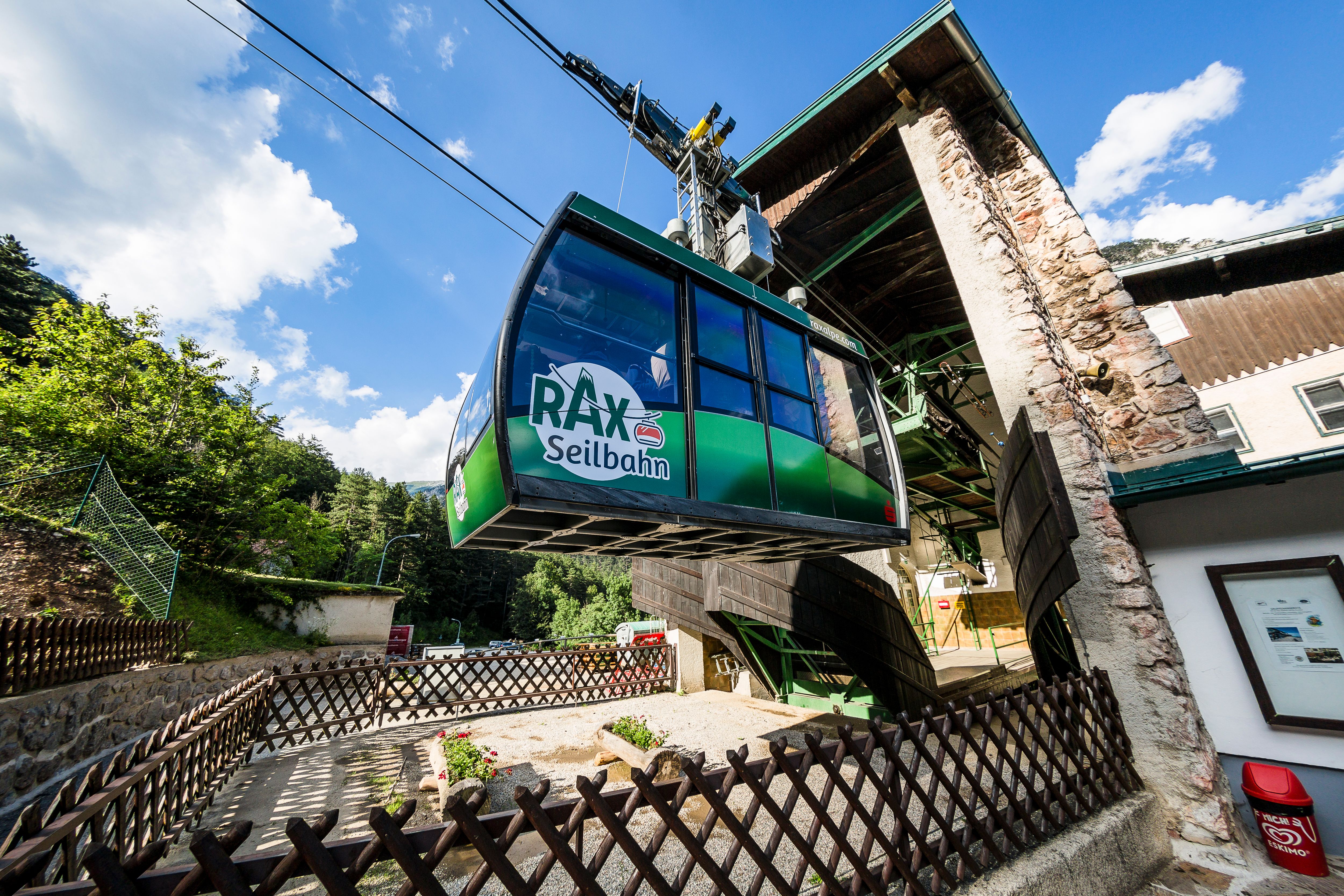 Rax cable car at the valley station, surrounded by trees and blue sky.